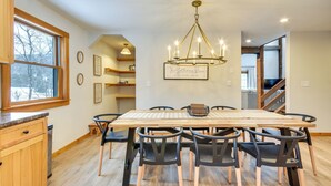 A dining area with a wooden table and chairs, a chandelier, and a view of a staircase. - Fish, Hike & Ski: Spacious Family Escape in Eden (Eden)