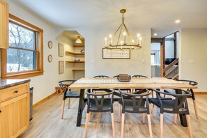 Un espace repas avec une table et des chaises en bois, un lustre et une vue sur un escalier.