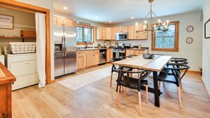 A modern kitchen with wooden cabinets, stainless steel appliances, and a dining area with black chairs. - Fish, Hike & Ski: Spacious Family Escape in Eden (Eden)