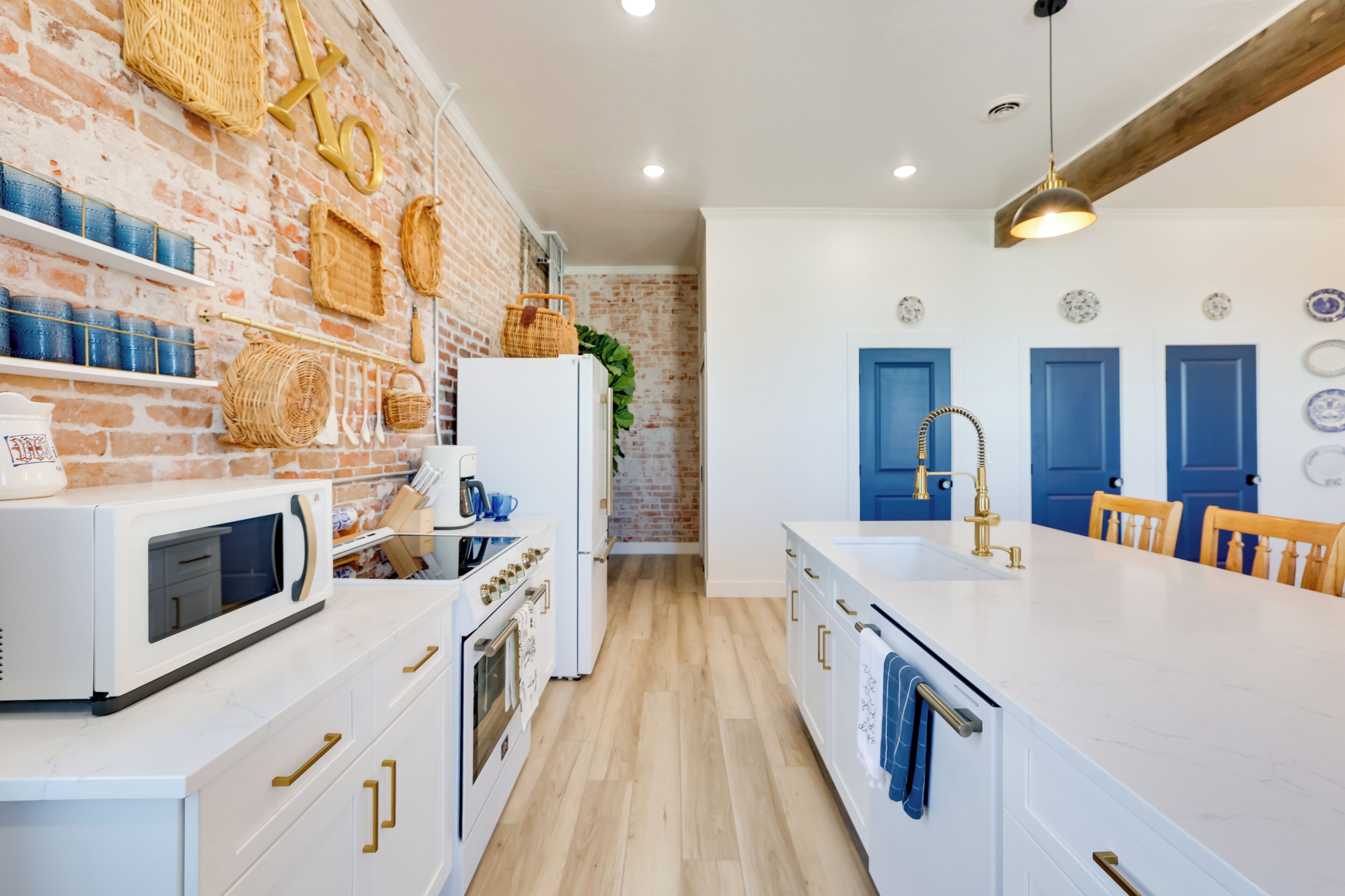 A modern kitchen with white cabinetry, a brick wall, and a large island with a sink.