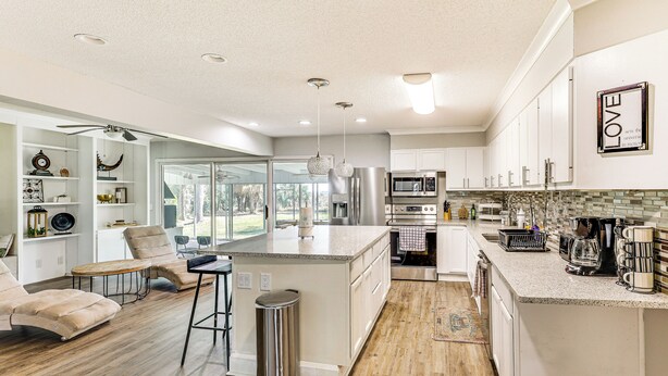 A modern kitchen with white cabinetry, a large island, and a dining area with a sofa and chairs. - 10 Mi to St Simons Island: Home w/ Screened Porch (Brunswick)