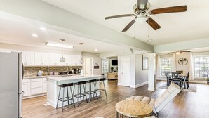 A spacious kitchen with a central island, bar stools, and a dining area with a round table and cushioned seating. - 10 Mi to St Simons Island: Home w/ Screened Porch (Brunswick)