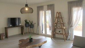 En stue med fjernsyn, sofabord i træ, potteplanter, en stigehylde og en hængende lampe.