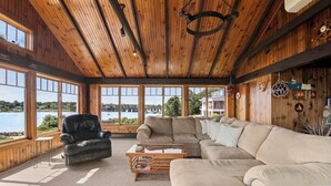 A spacious living room with a large sectional sofa, a leather armchair, and a wooden coffee table. The room features large windows offering a view of a body of water and buildings. - Stunning Waterfront Home! (Yarmouth)