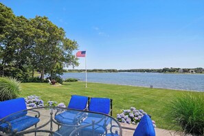 Eine Terrassenausrichtung am Seeufer mit einem Glastisch, blauen Stühlen, einer US-amerikanischen Flagge und Blick auf den See sowie die entfernte Uferlinie.