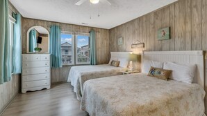 Une chambre avec deux lits, une commode, un ventilateur de plafond et une fenêtre avec des rideaux.