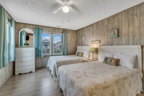 Een slaapkamer met twee bedden, een dressoir, een plafondventilator en een raam met gordijnen.