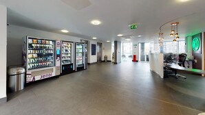A spacious lobby with vending machines, a reception desk, and a clear exit sign. - Sterling Court (Wembley)