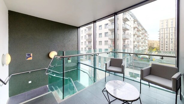 A modern interior with a glass balcony, a staircase, and a seating area with two sofas and a small table. - Sterling Court (Wembley)