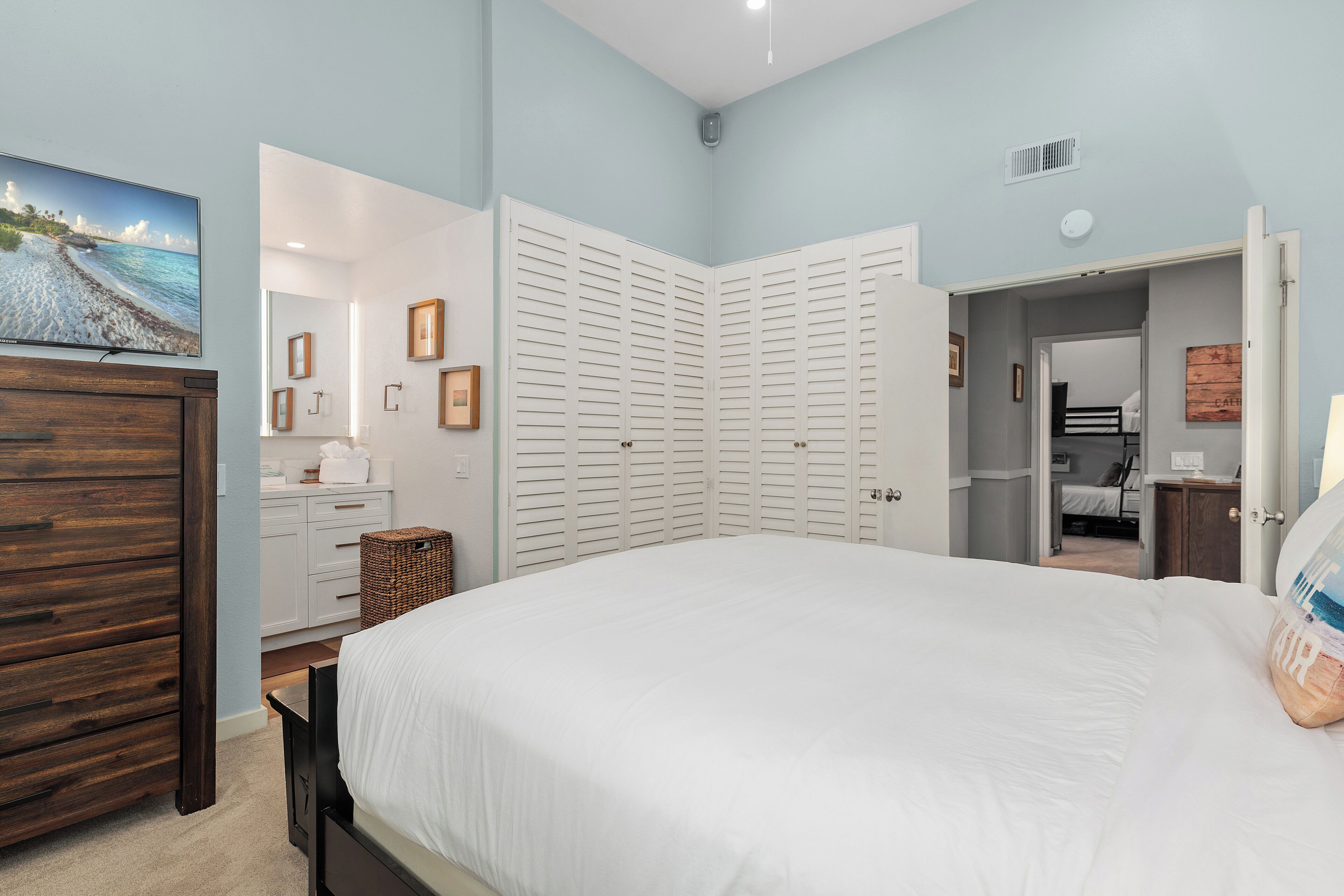 A bedroom with a large bed, a dresser, a TV, and a closet.