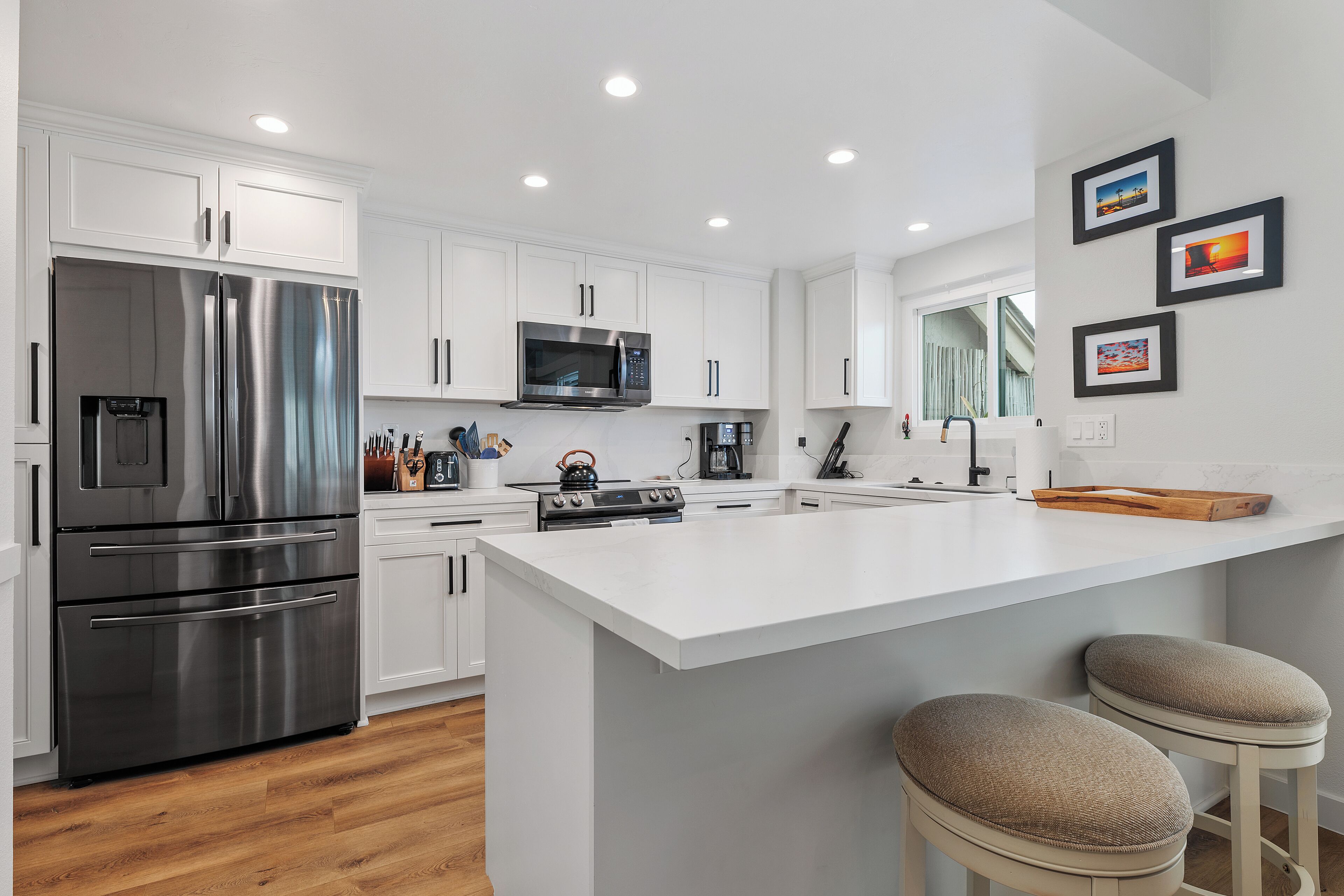 Una cocina moderna con armarios blancos, electrodomésticos de acero inoxidable y una isla central con taburetes de bar.