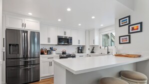 A modern kitchen with white cabinetry, stainless steel appliances, and a central island with bar stools.