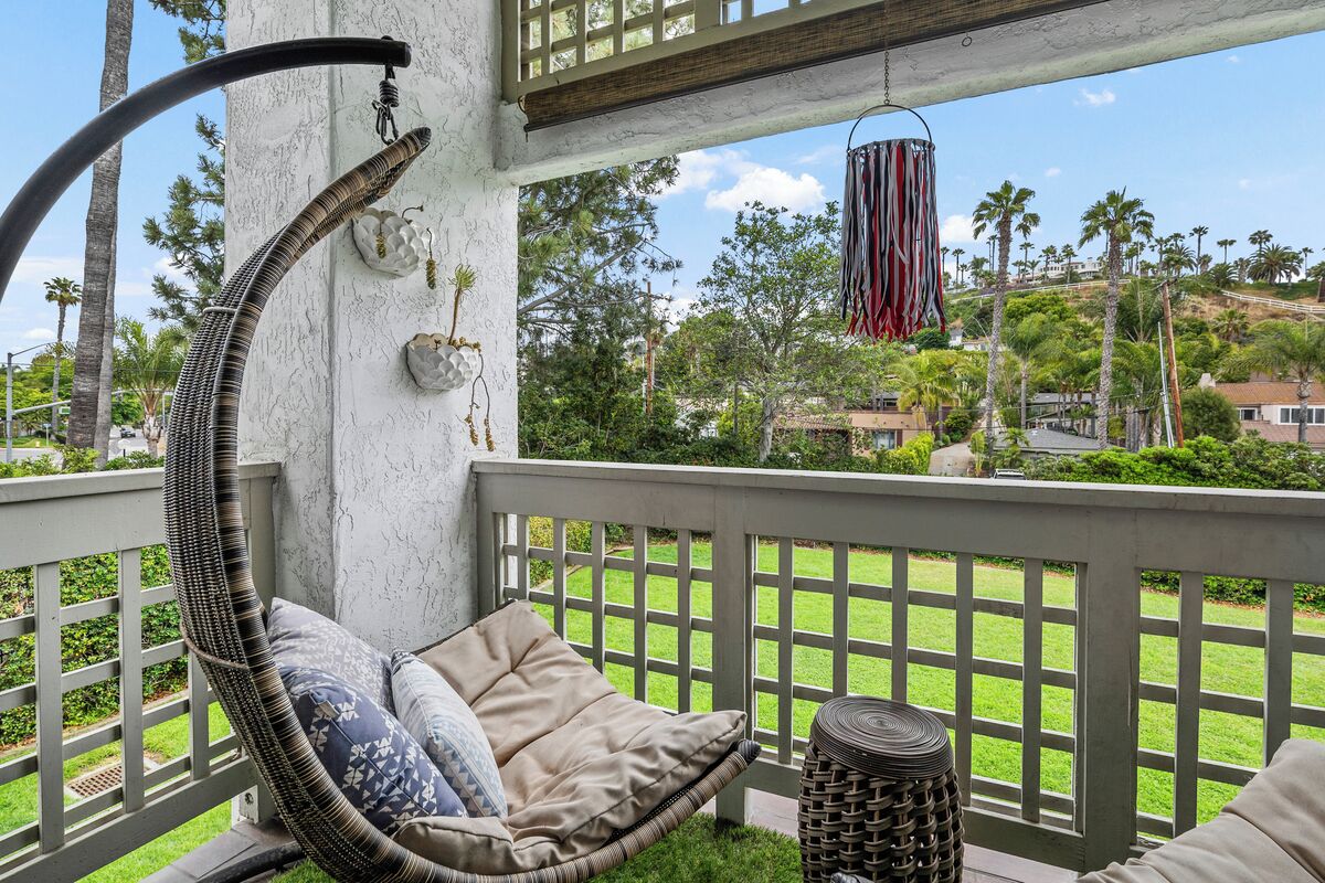 Una silla de mimbre con cojines, una cesta de mimbre y vistas a un césped verde y palmeras.