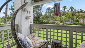 A wicker chair with cushions, a wicker basket, and a view of a green lawn and palm trees.