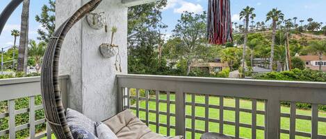 Una silla de mimbre con cojines, una cesta de mimbre y vistas a un césped verde y palmeras.