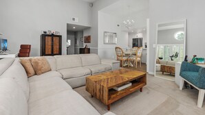 A spacious living room with a large sectional sofa, a wooden coffee table, and a dining area with chairs and a table.