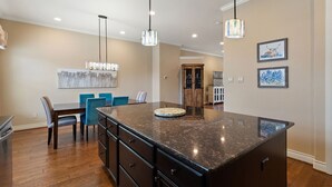 A modern kitchen with a large island, dark cabinetry, and blue chairs. - Bend in the River - Gorgeous 4-Level Brownstone with Rooftop Views (Georgetown)
