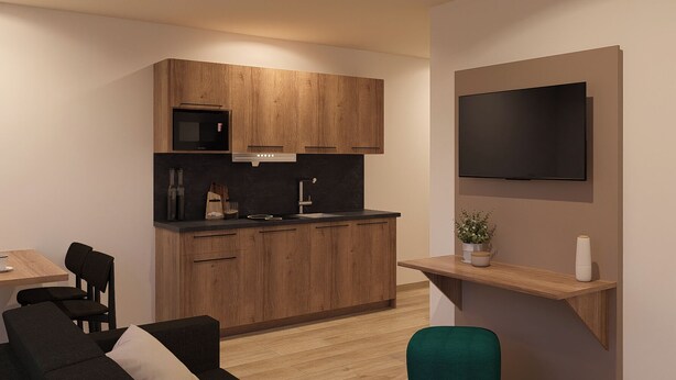 A modern kitchen with wooden cabinets, a black countertop, and a built-in oven. There is a dining area with a table and chairs, and a TV mounted on the wall. - Apartments by Simmerlwirt (Woergl)