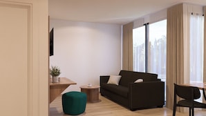 Un salon moderne avec un canapé foncé, une petite table ronde, un pouf vert et un téléviseur fixé au mur.