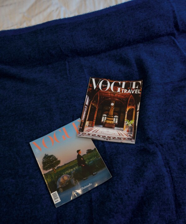 Two magazines, one titled 'VOGUE TRAVEL' and the other 'VOGUE', placed on a dark blue fabric surface. - Neon 45 Apartment - ProperUNIT (Wroclaw)