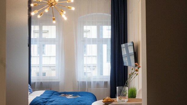 A bedroom with a bed, a desk, a chair, and a hanging light fixture. - Neon 45 Apartment - ProperUNIT (Wroclaw)
