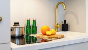 A kitchen with a stainless steel pot, green bottles, an orange, and a wooden cutting board on the counter. - Neon 45 Apartment - ProperUNIT (Wroclaw)
