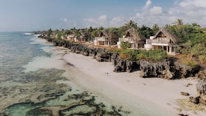 A beachfront resort with thatched-roof villas, clear turquoise waters, and a rocky shoreline. - Matemwe Attitude (Matemwe)