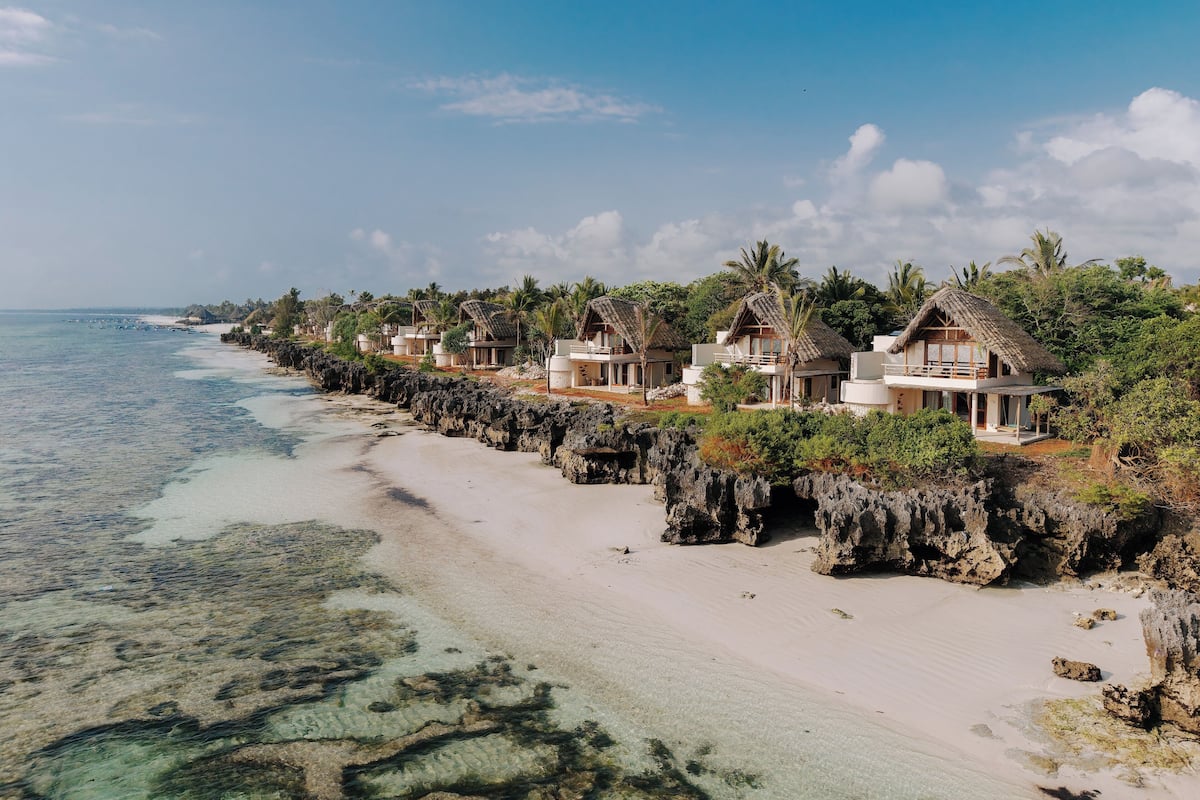 A beachfront resort with thatched-roof villas, clear turquoise waters, and a rocky shoreline.