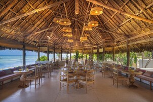 Un amplio espacio al aire libre con mesas y sillas de madera, rodeado por una estructura de techo de paja.