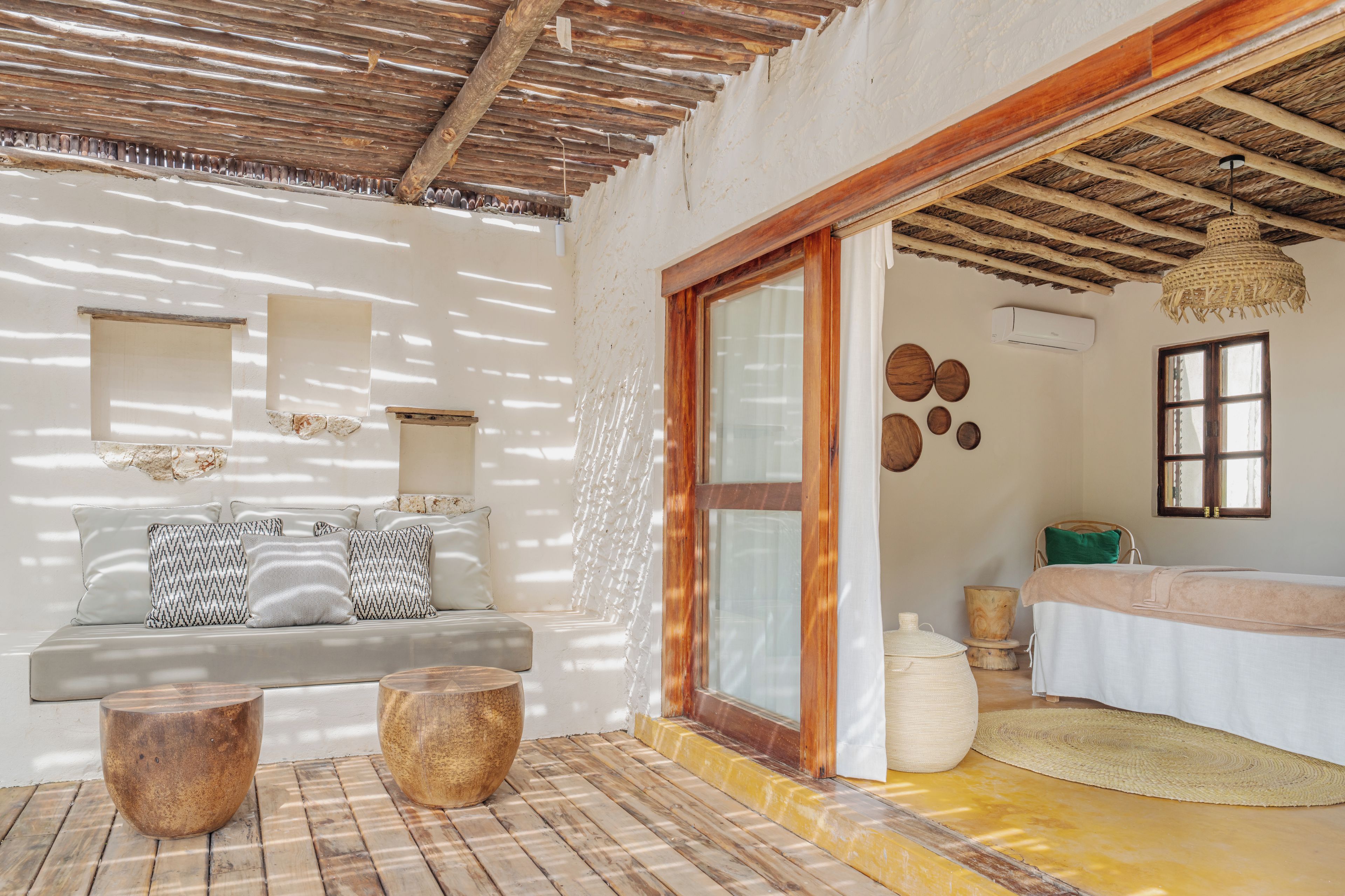 A room with a wooden ceiling, a sofa with patterned cushions, a wooden coffee table, and a large window with a view.