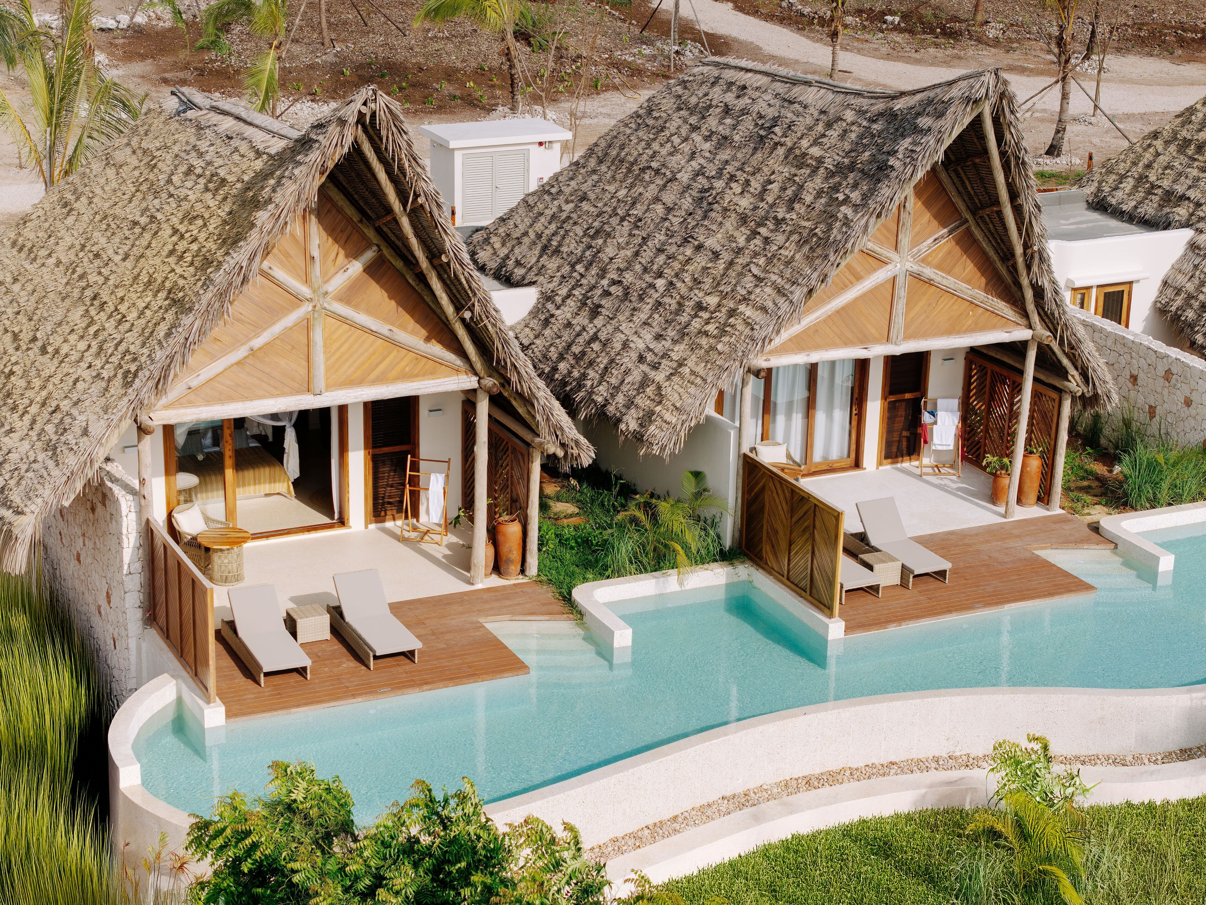 Un resort con cabañas de techo de paja, una piscina y zonas de descanso.