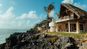 A beachfront property with a thatched-roof house, a stone wall, and a view of the ocean. - Matemwe Attitude (Matemwe)