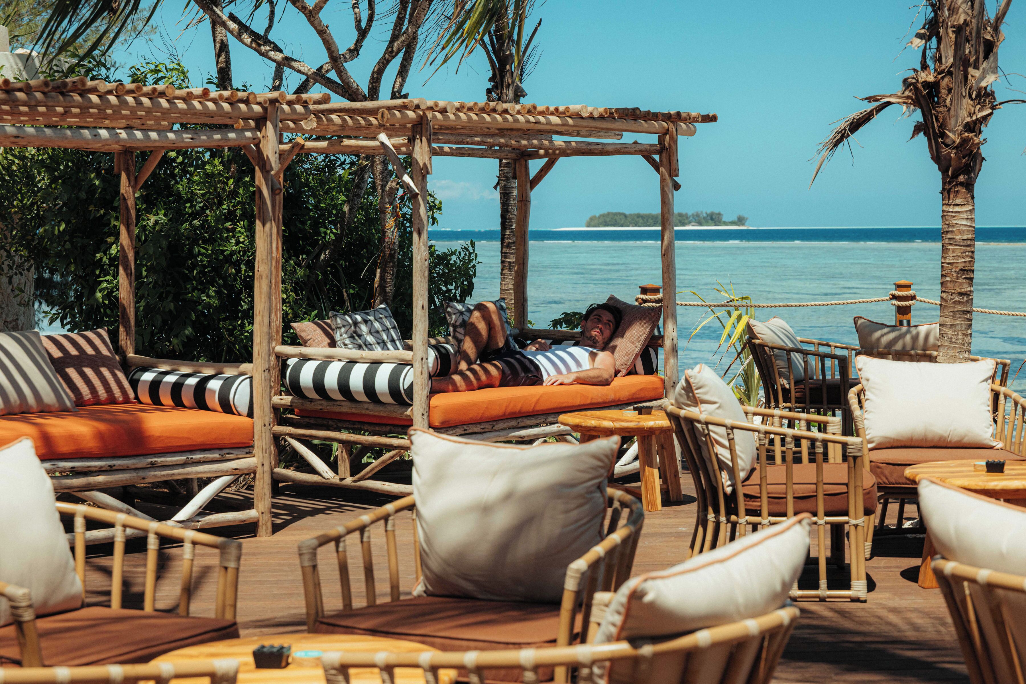Terraza de madera con mobiliario de mimbre, incluyendo sofás y sillones, con vista a un cuerpo de agua.