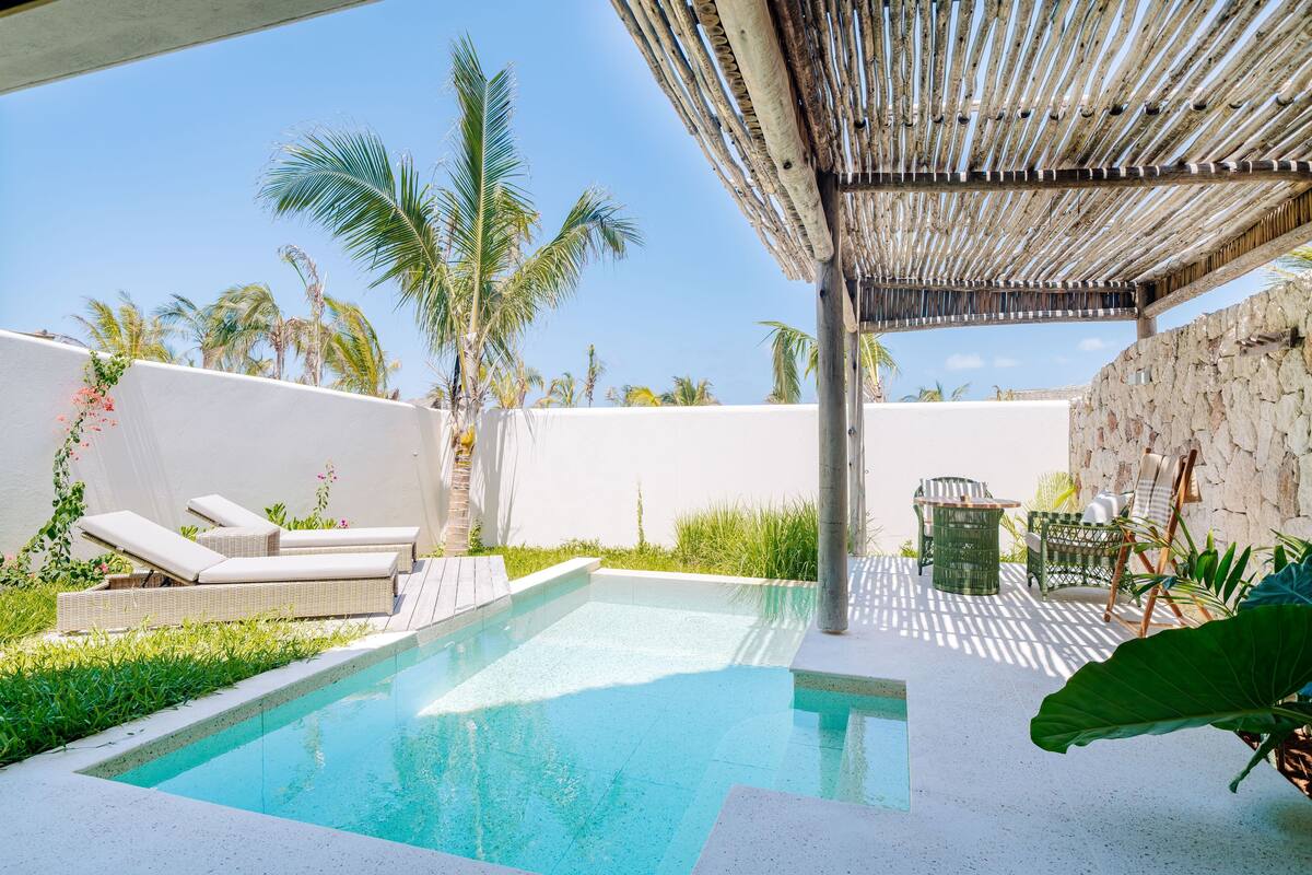 A pool area with lounge chairs, a pergola, and palm trees.