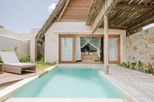 Un área junto a la piscina con una silla de descanso, una cama con dosel y un muro de piedra.