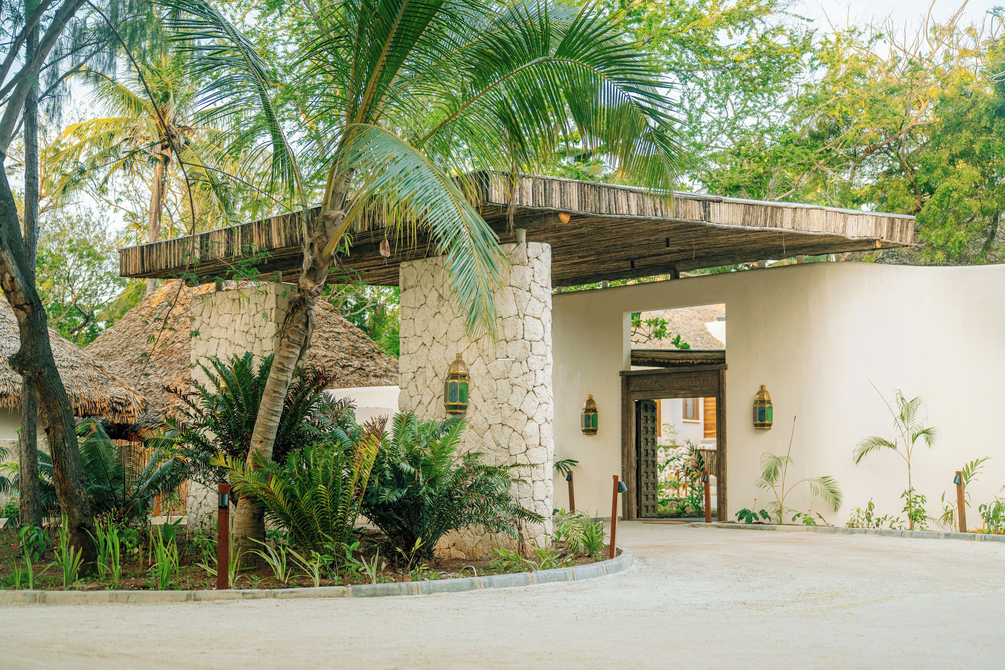 Un edificio con facciata in pietra, tetto di paglia e area d'ingresso pavimentata con piante.