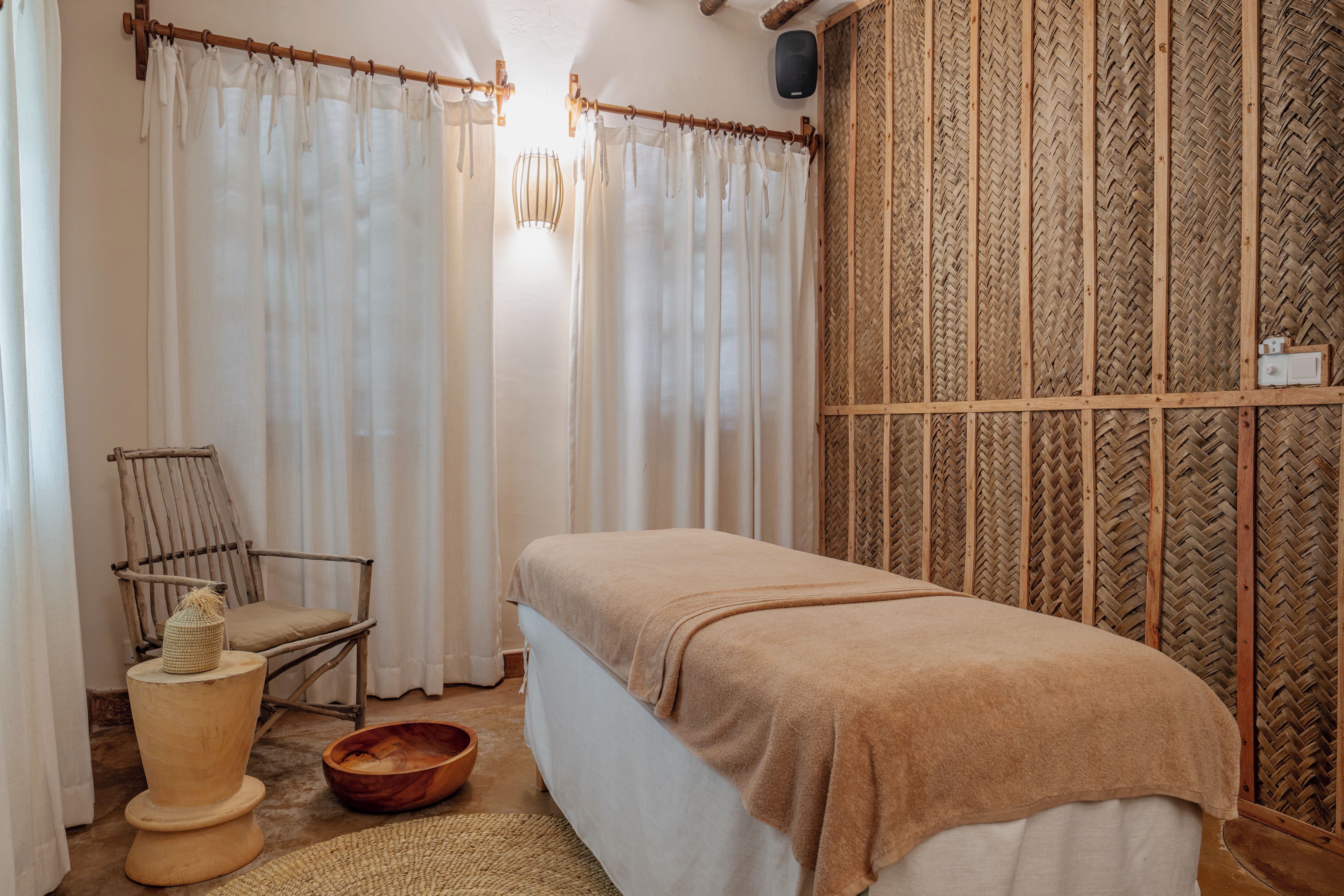 A room with a bed, a chair, a wooden bowl, and a woven wall panel.