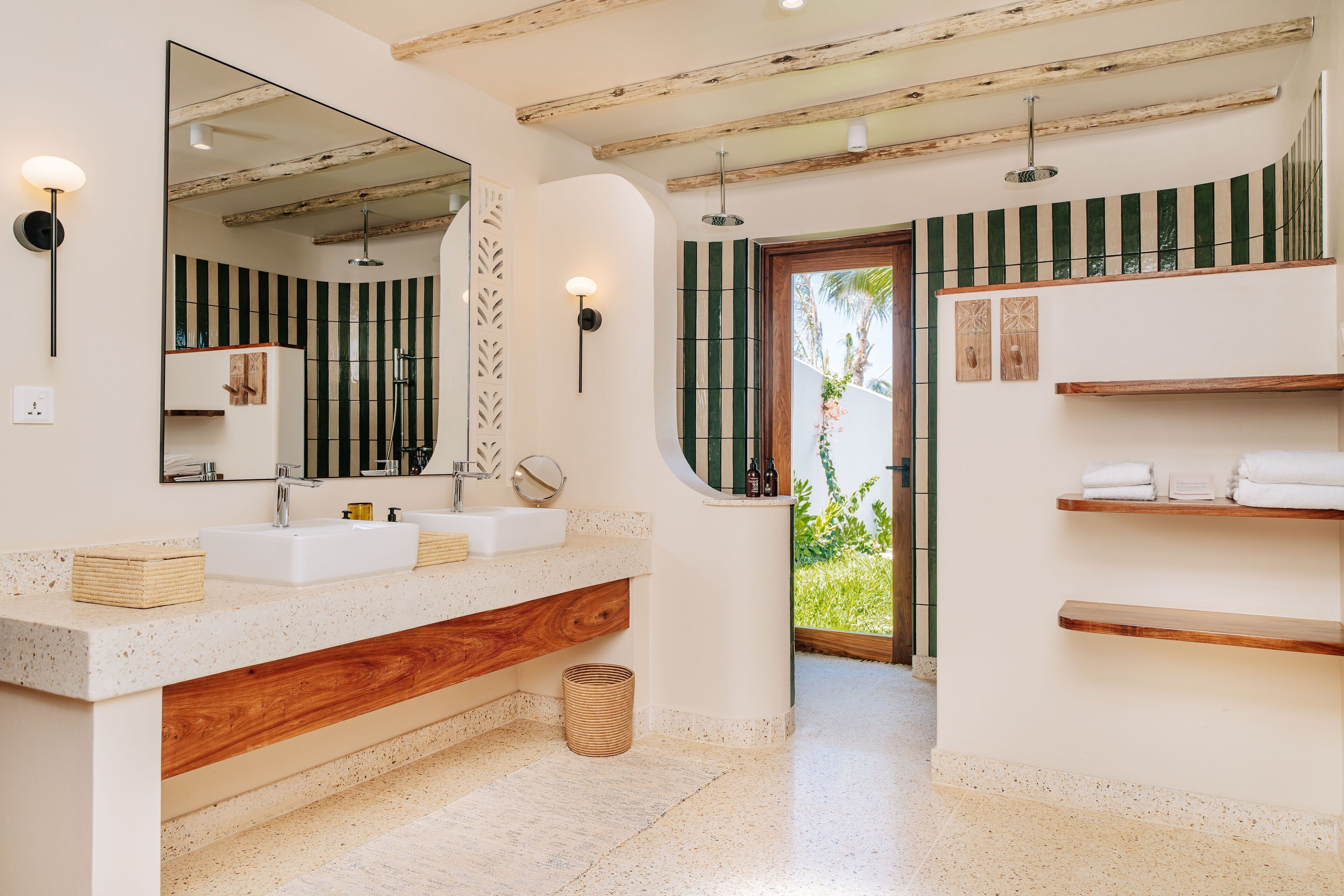 Un baño moderno con un espejo grande, dos lavamanos, estantes de madera y vista a zonas verdes.
