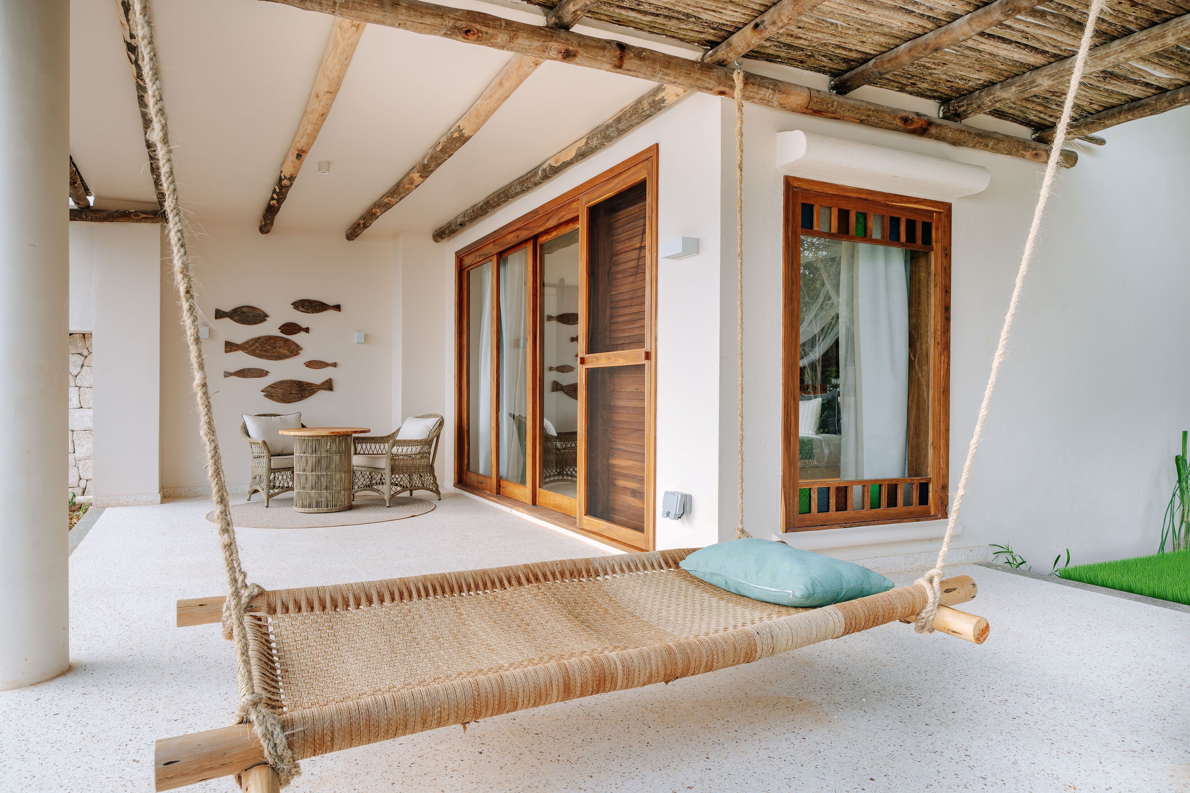 A hammock suspended from a wooden beam, a wicker table with chairs, and a glass door leading to an outdoor area.