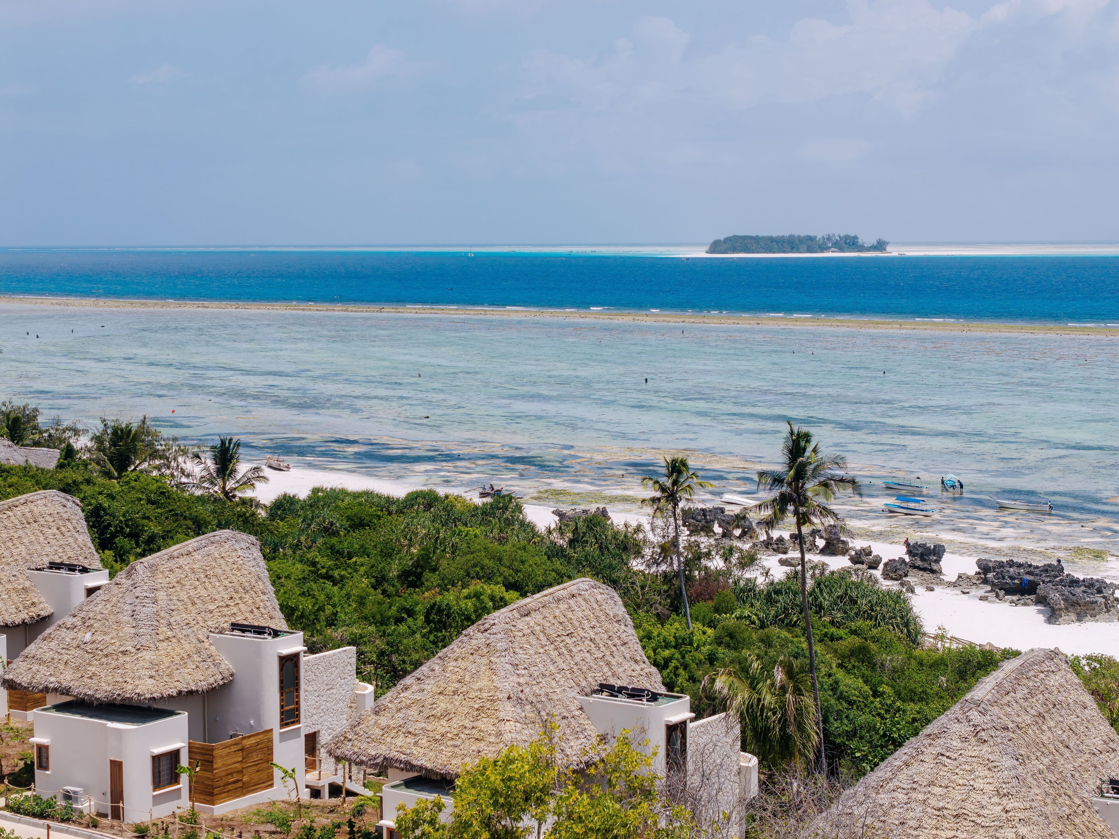 A coastal resort with thatched-roof bungalows, a sandy beach, and a clear view of the ocean.