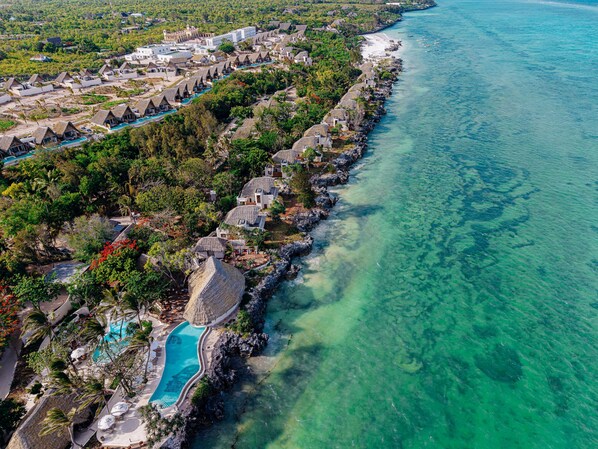 An aerial view of a coastal resort with multiple bungalow-style accommodations, a central swimming pool, and clear turquoise waters. - Matemwe Attitude (Matemwe)