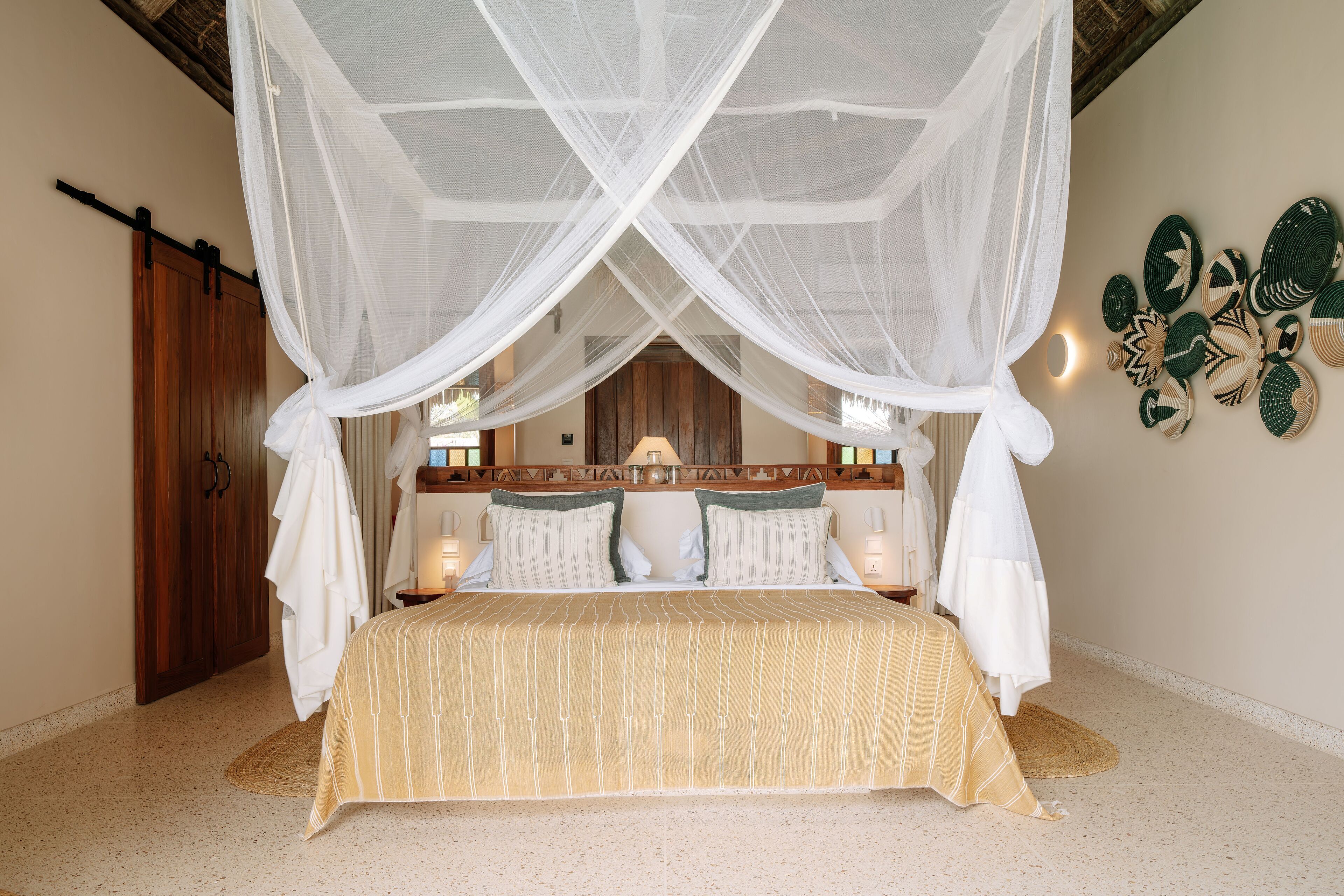 Una cama con dosel, cabecera de madera y un muro decorado con arte tejido.