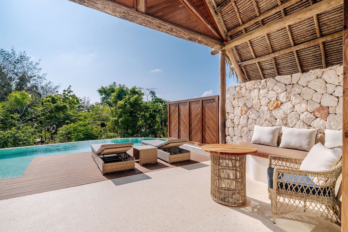 An outdoor pool area with wicker furniture and a stone wall.