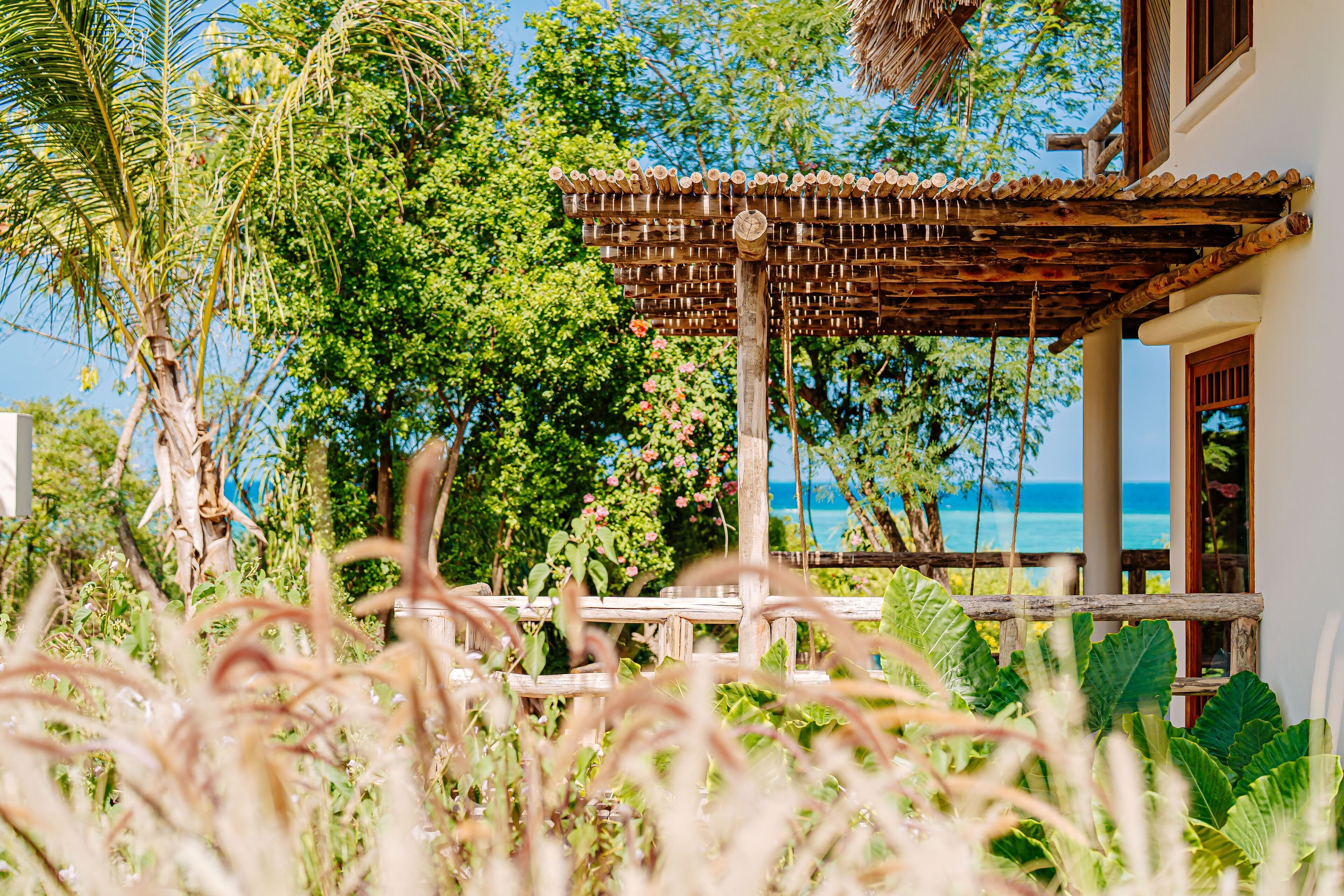 A wooden pergola with a thatched roof overlooking a lush garden and a view of the ocean.