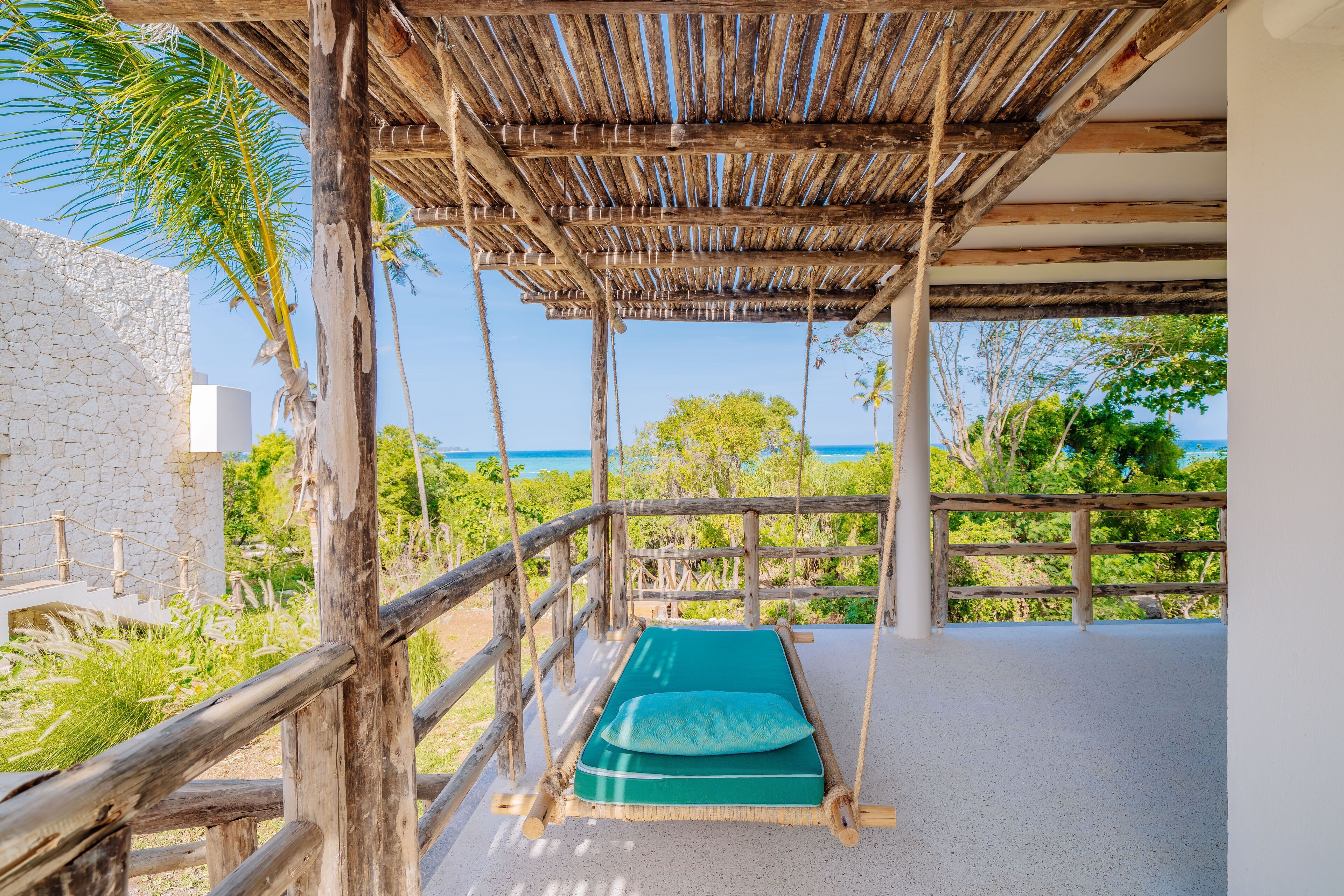 A hammock under a wooden pergola with a view of the ocean.