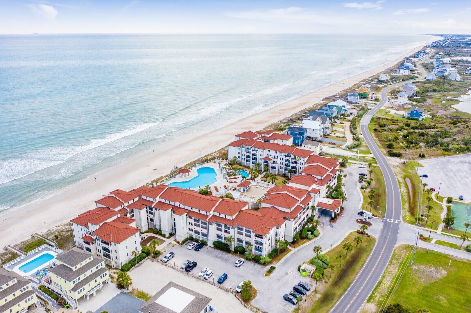 A coastal hotel with multiple buildings, a swimming pool, and a beach view.