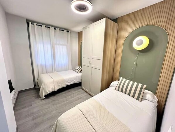 A bedroom with two beds, a wardrobe, and a unique circular light fixture on the wall. - Apartamento de 3 habitaciones en Rivas (Málaga)