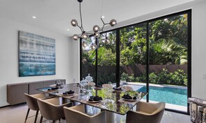 A modern dining area with a glass table, chairs, and a view of a swimming pool.