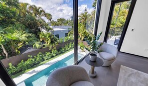 A modern interior with a large window overlooking a pool and lush garden.