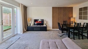 Un salón moderno con televisor de pantalla plana, una mesa de comedor con sillas y un amplio ventanal corredero que da a un área exterior.